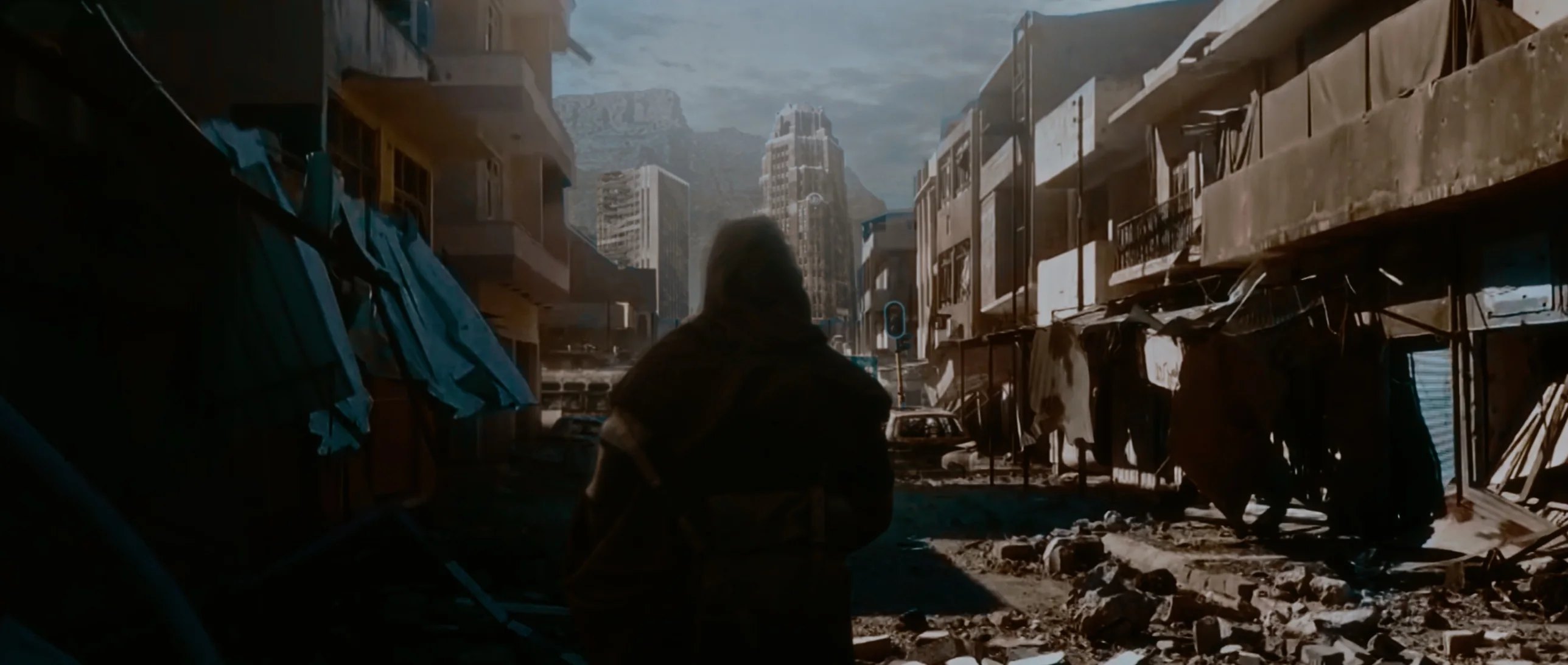 A hooded figure walking down a ruined street toward Table Mountain